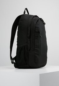 Zaino nero realizzato in tessuto resistente con una finitura texture. Presenta una tasca laterale in rete, una zip frontale e spallacci imbottiti.