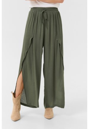 Olivgrüne weit geschnittene Hose aus strukturiertem Stoff, mit elastischem Bund und seitlichen Schlitzen. Kombiniert mit tanfarbenen Stiefeletten.