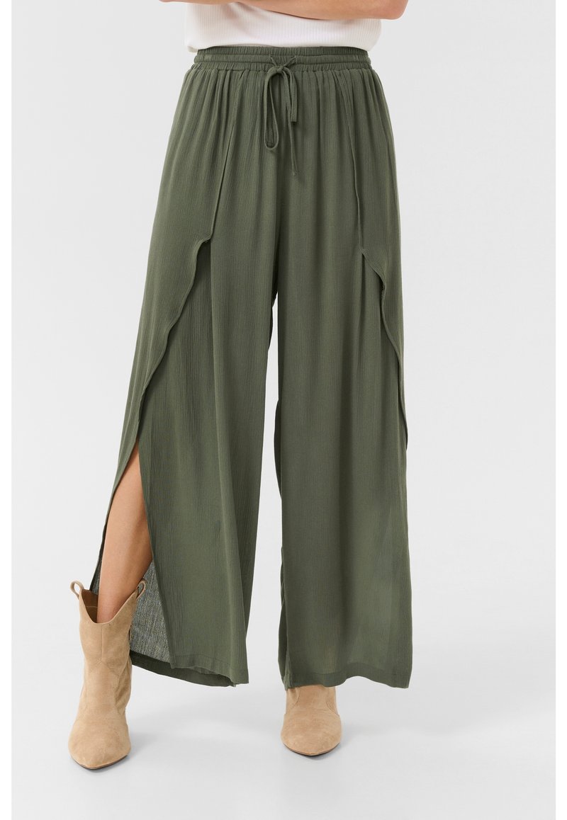 Pantaloni a gamba larga verde oliva in tessuto texturizzato, con vita elastica e fessure laterali. Abbinati a stivaletti alla caviglia di colore sabbia.