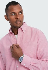 Vaaleanpunainen nappikauluspaita, joka on valmistettu tekstuurikankaasta, jossa on rintatasku ja valkoisia nappeja; yhdistettynä hopeiseen rannekelloon.