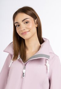 Jachetă de culoare roz deschis, cu guler înalt, accente gri, fermoar alb cu logo și broderie în formă de inimă pe piept. Textură moale, design casual.