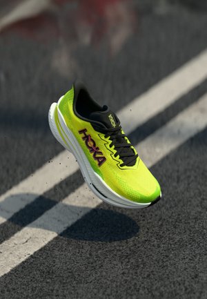 Hoka-Laufschuh mit einem hellen Neongelben Mesh-Obermaterial, schwarzen Akzenten und einer weißen Zwischensohle, die ein schlankes Design und eine strukturierte Oberfläche aufweist.