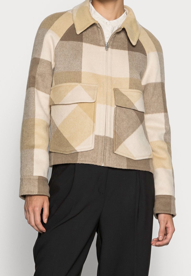 Ruskean ja beigen ruudullinen villatakki, jossa on kaulus, vetoketjusuljenta ja kaksi etutaskua; teksturoitu kangas kontrastoivilla kuoseilla.