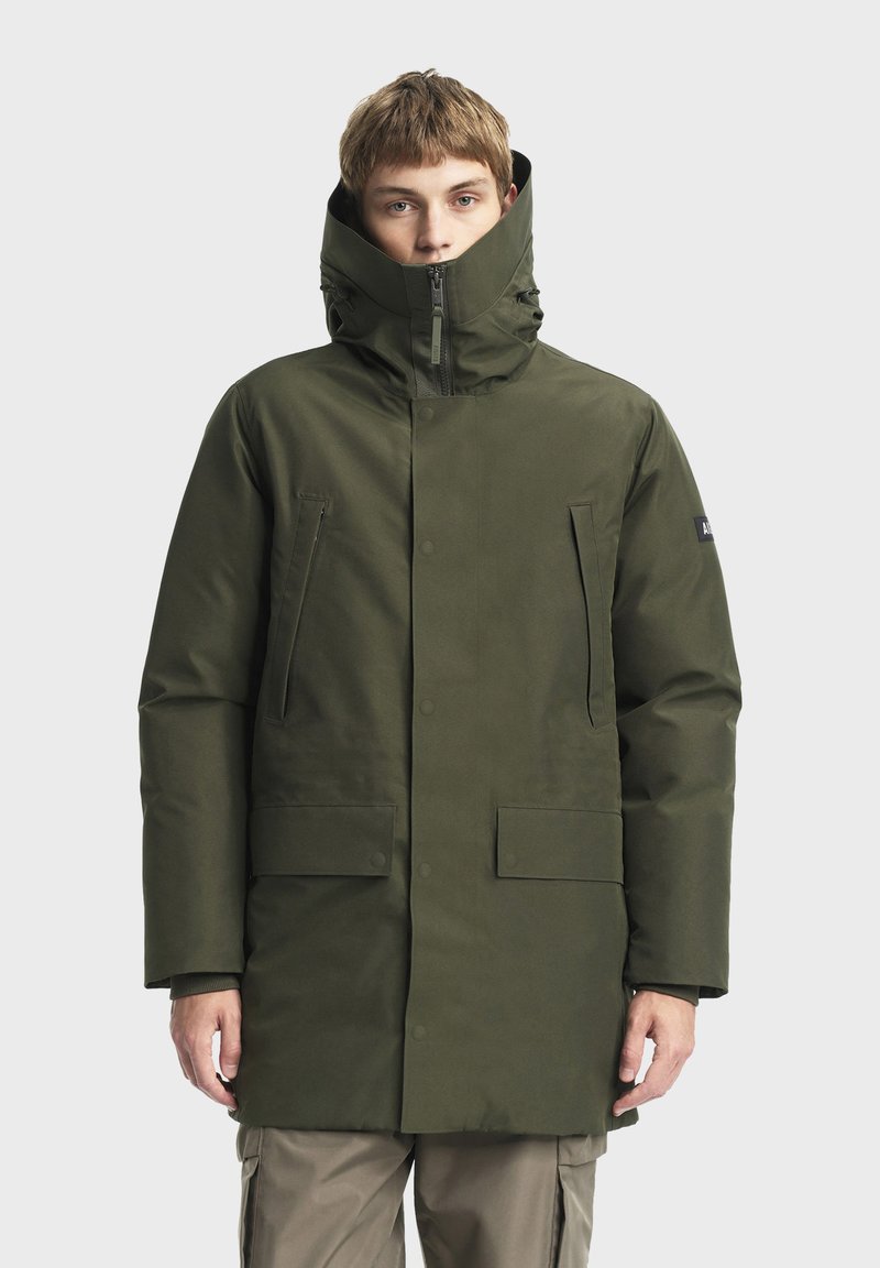 Parka verte en finition mate, dotée d'un col haut, d'une fermeture éclair, de poches latérales et d'une forme rectangulaire pour la chaleur et la protection.