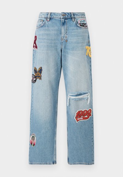 Lyseblå denimjeans med ulike lapper, et slitt kne og bred benpassform. Merkbare farger inkluderer rød, gul og svart.