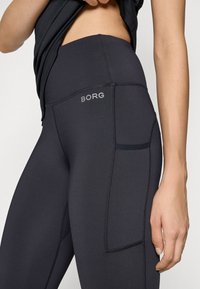 Juodos aukštos liemens leggingai su šonine kišene, pasiūti iš lygaus, tampraus audinio ir turintys pilką "BORG" logotipą ant juosmens.