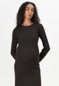 Abito maglione a coste marrone con maniche lunghe, scollo rotondo e silhouette attillata, caratterizzato da una texture morbida e da un motivo a strisce verticali.