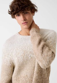 Maglione beige e crema con blocchi di colore e finitura a lavorato testurizzato. Le maniche sono leggermente a sbuffo, evidenziando un tessuto soffice e accogliente.