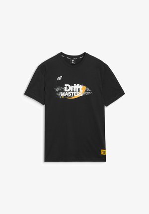 Mężczyzna w czarnej czapce "Drift Masters" i pasującej czarnej koszulce z białym i żółtym napisem na jednolitym tle.