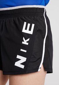 Mustat urheilushortsit, jotka on valmistettu kevyestä kankaasta, joissa on valkoinen Nike-brändäys, kontrastiväriset sivuraidat ja teksturoitu kuvio.