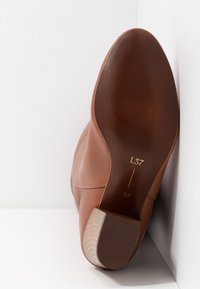 Chaussure en cuir marron montrée semelle vers le haut sur fond blanc, affichant la taille 37 et un talon avec une semelle en caoutchouc texturée.