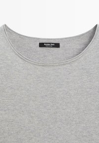 Jasnoszary sweter z okrągłym dekoltem z czarną metką z napisem „Massimo Dutti MADE IN CHINA” na środku kołnierza.