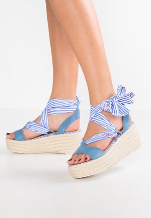 Blue espadrille wedge sandals with striped fabric straps. Features include a woven jute sole and a knotted accent on the ankle.