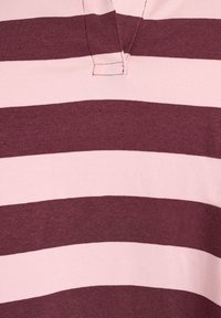 Rozā un bordo svītrainā T-kreklā, izgatavotā no mīkstas kokvilnas savienojuma, ar nelielu V veida kakla izgriezumu un īsām piedurknēm, ar redzamām šuvju detaļām.