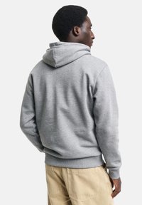 Gray hoodie made of soft fabric, featuring a drawstring hood, ribbed cuffs, and hem, paired with beige pants showing pockets.