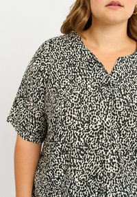 Blusa a maniche corte con scollo a V, a fantasia bianco e nero, realizzata in un tessuto morbido e leggero, con forme astratte irregolari.