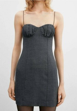 Femme portant une mini-robe moulante sans manches gris foncé avec de fines bretelles spaghetti et des détails plissés sur le buste.