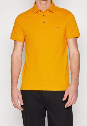 Gelbes Poloshirt mit Kragen, kurzen Ärmeln und zwei Knöpfen am Ausschnitt. Mit kleinem Logo auf der linken Brust. Baumwollmaterial.