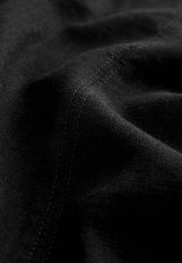 Tissu noir à surface texturée, présentant un léger éclat et des coutures contrastées. Le matériau semble doux et légèrement drapé.