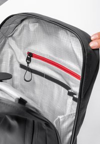 Zaino nero con interno grigio caratterizzato da un motivo a griglia, tasca con cerniera rossa e un gancio per chiavi o accessori.