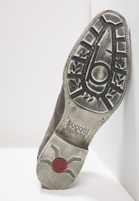 Chaussure en cuir gris avec une semelle en caoutchouc texturée arborant un motif de feuille, logo visible et accent rouge sur un talon arrondi.