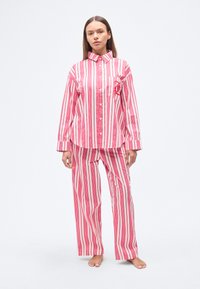 Ροζ και λευκό ριγέ σετ πυτζάμας με πουκάμισο με κουμπιά και τσέπη, συνοδευόμενο από άνετο παντελόνι. Λείο βαμβακερό ύφασμα.