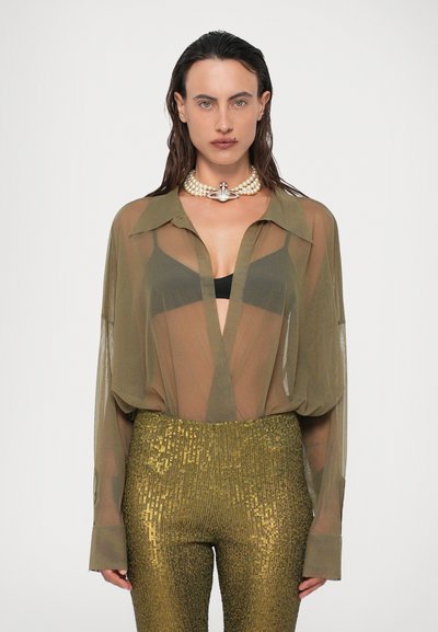 Olivovo zelená priesvitná košeľa na gombíky s vyrolovanými rukávmi, spárovaná s zlatými flitrovými priliehavými nohavicami. Na krku je perlový a kryštálový náhrdelník.
