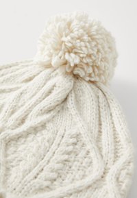 Berretto lavorato a maglia bianco con un motivo texture e un pompon soffice sulla parte superiore. Il materiale sembra morbido e spesso, adatto per mantenere caldo.