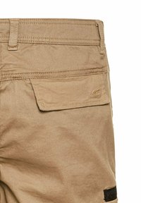 Beige short met een gladde textuur, met een achterzak en contrasterende stiksels. Het ontwerp bevat een subtiele logodetail.
