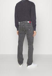 Grå denim jeans med smalnande ben, två bakfickor och en logotyprem. Matcher med en mörk sweatshirt och vita sneakers.