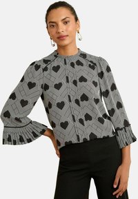 Blusa a maniche lunghe bianco e nero con motivo geometrico a cuore, con polsini arricciati e una scollatura alta per un design strutturato.