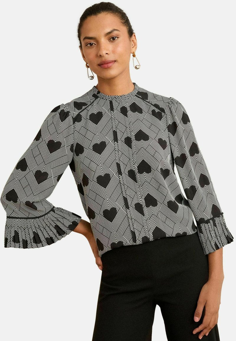 Blusa a maniche lunghe bianco e nero con motivo geometrico a cuore, con polsini arricciati e una scollatura alta per un design strutturato.