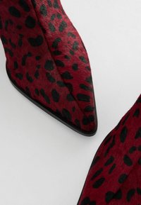 Cipele s visokom petom u leopardskom uzorku u crvenoj i crnoj boji, s oštrim vrhom i teksturom krzna, te glatkim crnim đonom.