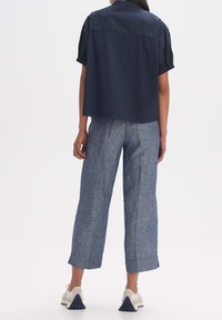 Camisa corta de marina con mangas cortas abullonadas, combinada con pantalones anchos y texturizados de color azul claro. Zapatillas blancas con acentos azules completan el conjunto.