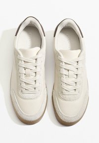 Kermanvalkoiset lenkkitossut, joissa on sileä nahkainen päällinen ja mokkanahkaiset yksityiskohdat. Varustettu valkoisilla nauhoilla ja kuvioidulla kumipohjalla.