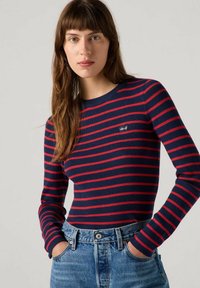 Roter und marineblauer gestreifter Rippshirt mit langen Ärmeln und rundem Halsausschnitt sowie kleinem Levi's-Logo auf der Brust. Getragen mit hochtaillierten Jeans.