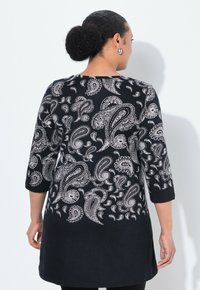 Schwarze Tunika mit weißem Paisleymuster, 3/4-Ärmeln, runder Ausschnitt und abgerundetem Saum. Hergestellt aus einem weichen Stoff mit glatter Textur.