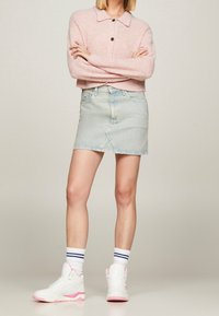Jasnoróżowy sweter z dzianiny z kołnierzykiem i detalami guzików, połączony z jasnoniebieską spódnicą dżinsową o skośnym wykończeniu. Białe trampki za kostkę z różowymi akcentami.