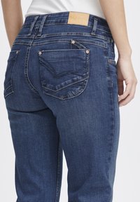 Vaqueros de mezclilla azul oscuro con corte recto, con un parche de cuero en la cinturilla y bolsillos traseros cosidos doblemente.