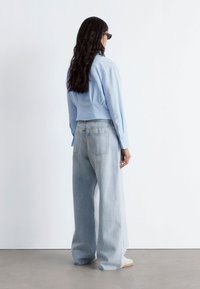 Light blue cropped shirt paired with loose, light-wash denim jeans. The shirt features long sleeves; the jeans have a classic five-pocket design.