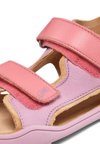Sandalia de cuero rosa claro con una correa rosa suave, acentos texturizados, lados abiertos y suela tipo corcho. Cierre de velcro para un ajuste ajustable.