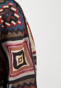 Tela tejida multicolor con patrones geométricos en rojo, azul y marrón. Presenta una textura detallada y un borde negro.