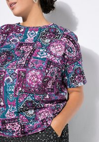 Krátký rukáv top s živým patchwork vzorem v růžové, azurové a černé barvě, vyrobený z hladkého materiálu s volným střihem.
