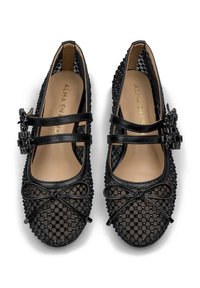 Zapatos de bailarina de malla negra con dos correas, un patrón texturizado, detalle de lazo en la parte frontal y un forro interior suave. Presenta acabados glossy.