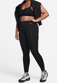 Černá sportovní podprsenka a legíny s vysokým pasem vyrobené z pružného materiálu. Tento outfit je doplněn černými a bílými sportovními botami.