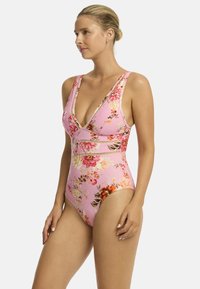 Różowy kostium kąpielowy w kwiaty z dekoltem w serek, szerokimi ramiączkami i dopasowanym krojem. Posiada żywe kwiaty i poziome akcenty.