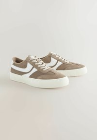 Brune ruskindsneakers med hvide accenter, der har et lavt design, rund tå og flad gummisål. Snørebånd i matchende farve.