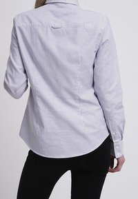 Randig skjorta i blått och vitt, med långa ärmar, krage och rundad nederkant. Tyget verkar vara slätt med en figurnära design.