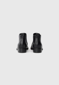 Bottines en cuir noir avec une texture lisse, dotées d'un petit talon et d'une tirette à l'arrière pour un enfilage facile.