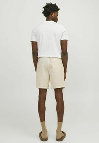 Rövid, bézs árnyalatú, bordázott textúrájú rövidnadrág, elasztikus derékkal és hátsó zsebbel. Egyszerű fehér pólóval és barna zoknikkal viselve.